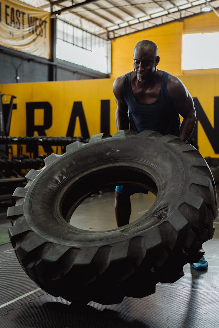 Strong man flipping heavy tire in an industrial gym environment, showcasing strength and fitness.